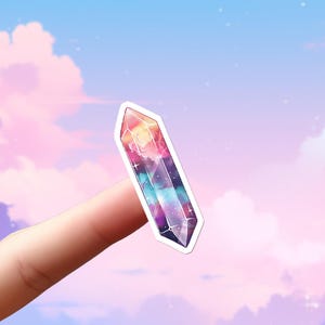 May include: A die-cut sticker shaped like a double-terminated crystal point. The sticker features a vibrant galaxy print with swirling shades of pink, purple, blue, and black, accented with small white stars and sparkles against a white border.