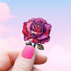 May include: A pink and purple galaxy rose sticker with a green stem and leaves. The sticker is being held by a hand against a pastel pink and blue sky background.