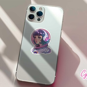 May include: A sticker featuring a cartoon illustration of a girl with purple hair wearing a white astronaut suit and headphones. The background is a pink and purple galaxy. The sticker is on a white iPhone.