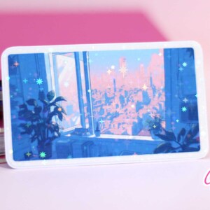 Puede incluir: Una pegatina que muestra una vista de la ciudad desde una ventana, con un esquema de color azul y rosa. La pegatina tiene un acabado hologr&aacute;fico con detalles de purpurina.