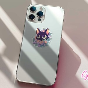 May include: A white iPhone with a black cat sticker on the back. The sticker features a black cat with large eyes and a floral design. The phone is on a white surface.
