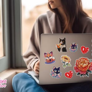 以下が含まれることがあります： 漫画の猫、キツネ、花、そして「Love」の文字が描かれたカラフルなステッカーで覆われたラップトップ。ステッカーは様々なサイズとデザインで、ラップトップの表面に装飾的なタッチを加えています。
