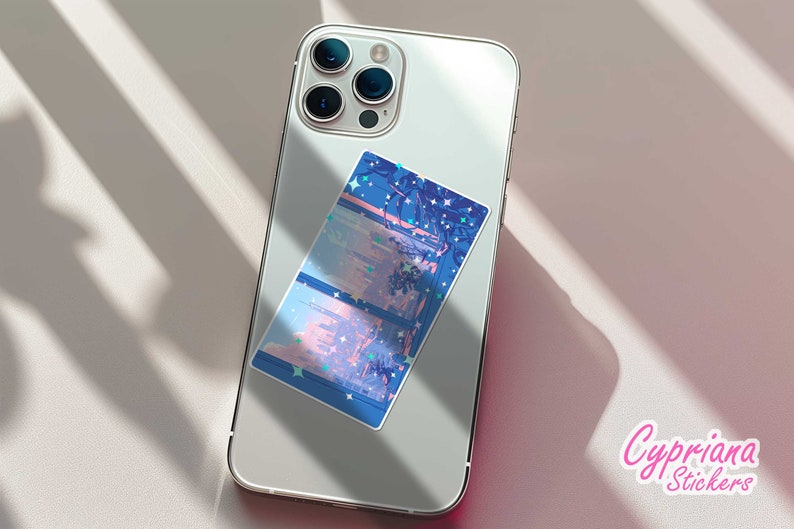 May include: A white iPhone with a blue and pink sticker on the back. The sticker features a cityscape with stars and a pink sky. The text "Cypriana Stickers" is printed in pink on a white background.