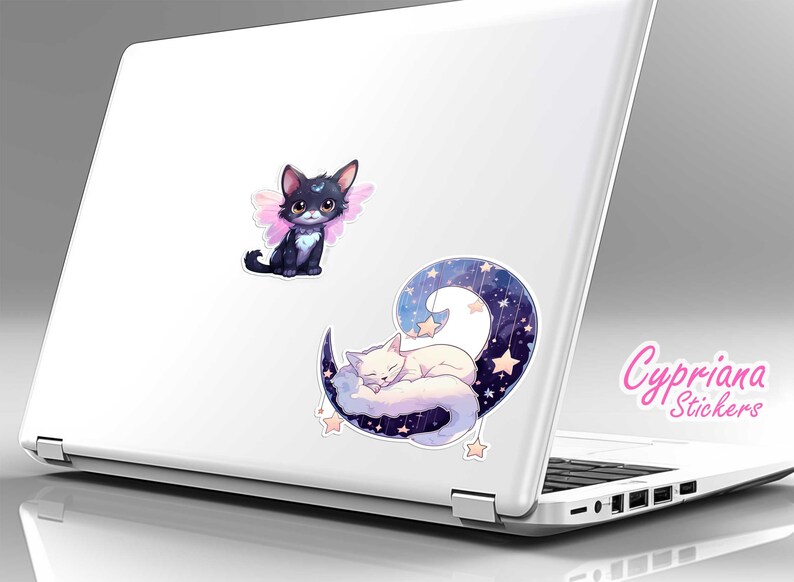 May include: Two cute cat stickers on a white laptop. One sticker features a black cat with pink wings and the other sticker features a white cat sleeping on a crescent moon with stars.