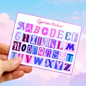 Könnte beinhalten: Ein Stickerbogen mit dem Alphabet in verschiedenen Pink-, Lila- und Blautönen. Die Buchstaben sind in einer kräftigen, stilisierten Schriftart gehalten, jeweils in einem Quadrat. Der Bogen ist mit "Cypriana Stickers" in Kursivschrift beschriftet.