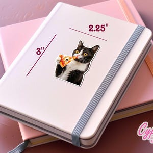 以下が含まれることがあります： 白のノートに、ピザを食べる白黒猫の7.6cmのステッカー。ステッカーの幅は5.7cmです。ノートはピンクのノートの上にあります。画像には「Cypriana Stickers」というテキストが含まれています。