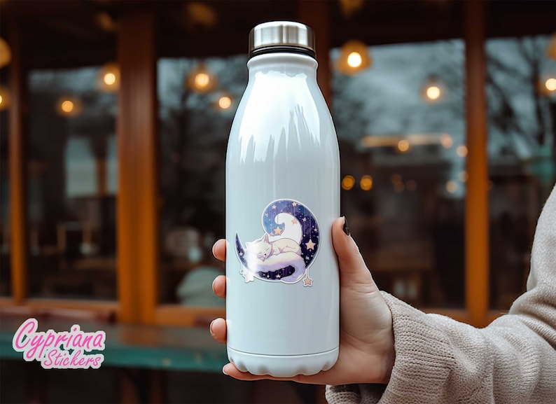 May include: White stainless steel water bottle with a sticker of a white cat sleeping on a crescent moon with stars. The sticker has a purple, blue, and white colour scheme.