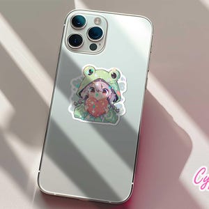 Pode incluir: Um adesivo para capa de telefone com tema de sapo verde com um personagem de desenho animado segurando um cora&ccedil;&atilde;o. O personagem tem cabelo rosa e est&aacute; usando uma fantasia de sapo verde. O adesivo est&aacute; em uma capa de telefone branca.