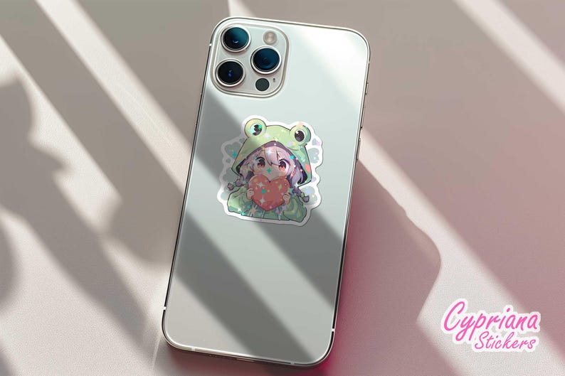 Pode incluir: Um adesivo para capa de telefone com tema de sapo verde com um personagem de desenho animado segurando um cora&ccedil;&atilde;o. O personagem tem cabelo rosa e est&aacute; usando uma fantasia de sapo verde. O adesivo est&aacute; em uma capa de telefone branca.