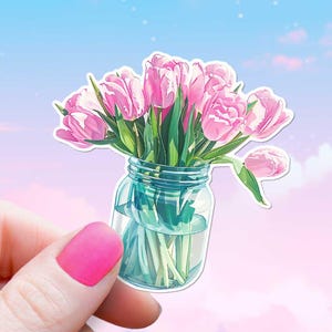 Op de afbeelding: Een boeket roze tulpen in een glazen pot. De tulpen zijn in een vaas met een lichtblauwe achtergrond gerangschikt.