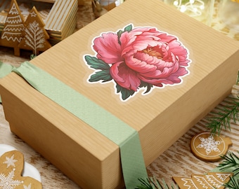 May include: A brown gift box with a green ribbon and a pink peony flower sticker. The box is sitting on a wooden surface with pine branches and gingerbread cookies.