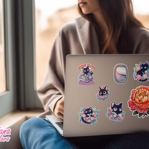 May include: A laptop computer with several stickers featuring black cats in flowers, a flower, and a window scene. The text on one sticker reads "Every Place Is a Garden".