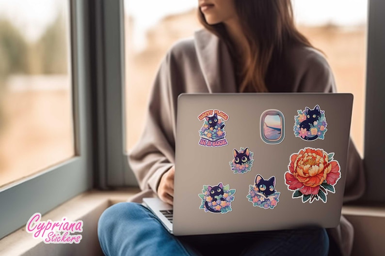 May include: A laptop computer with several stickers featuring black cats in flowers, a flower, and a window scene. The text on one sticker reads "Every Place Is a Garden".