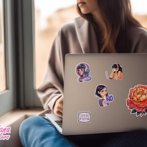 May include: A silver laptop computer with several stickers on the lid. The stickers feature illustrations of people wearing headphones, a flower, and text that says "I keep part of my routine".
