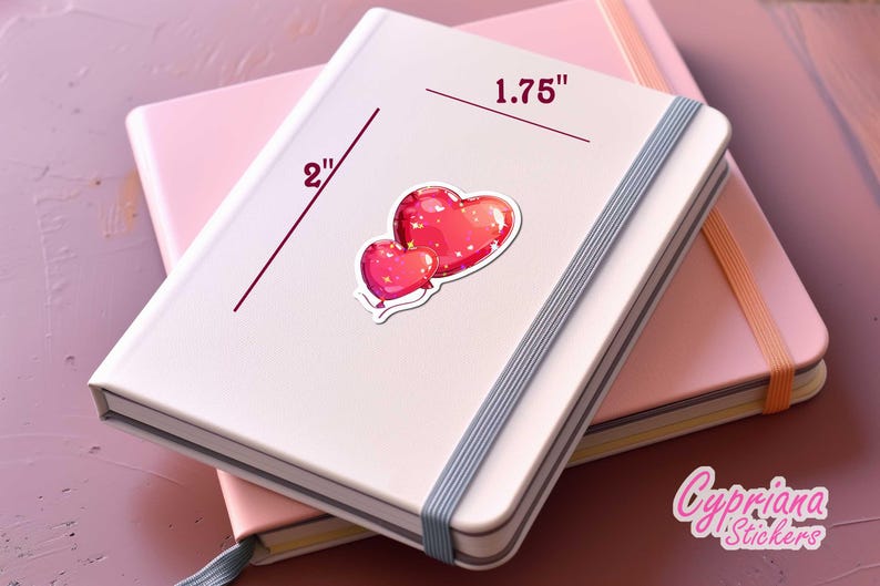 Peut inclure: Un carnet blanc avec un autocollant de deux coeurs rouges. L'autocollant est sur un carnet rose. L'autocollant mesure 4,4 cm de large. Le carnet a une bande &eacute;lastique grise.