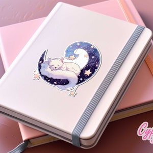 May include: A white fox curled up and sleeping on a crescent moon with a starry sky background. The sticker is on a pink and white notebook.