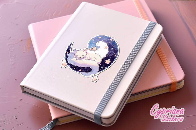 May include: A white fox curled up and sleeping on a crescent moon with a starry sky background. The sticker is on a pink and white notebook.