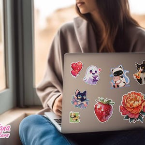 Peut inclure: Un ordinateur portable orn&eacute; d'autocollants color&eacute;s. On y trouve un c&oelig;ur rouge, un fant&ocirc;me, un panda avec un cochon, un chat noir et blanc mangeant une pizza, un chat noir dans des fleurs, une fraise et une grande fleur.