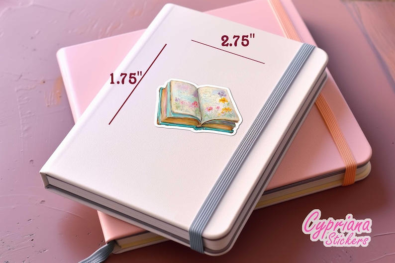 May include: A sticker of an open book with floral illustrations, measuring 2.75 inches wide and 1.75 inches tall, is placed on a white notebook. The notebook is on top of a pink notebook. The sticker has a watercolor style.