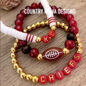 Könnte beinhalten: Drei Armbänder mit roten und goldenen Perlen, einer rot-weiß gestreiften Perle, einem Fußball-Anhänger und roten Perlen mit goldenen Buchstaben, die "CHIEFS" und "KC" buchstabieren.
