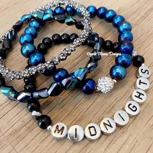 May include: Four blue and black beaded bracelets with a silver charm bracelet spelling out the word "MIDNIGHT" with a silver charm in the center.