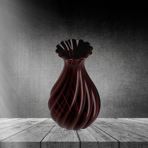 May include: A dark red glass vase with a swirling design. The vase has a wide mouth and a narrow base. It is sitting on a wooden surface.
