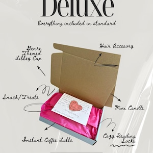 May include: A brown cardboard gift box with bright pink tissue paper inside, containing a white note with a red heart illustration. Text labels point to items including a Libbey cup, hair accessory, mini candle, snacks, and instant coffee latte.
