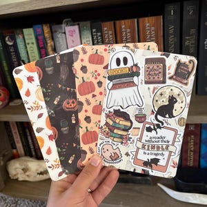 Puede incluir: Un conjunto de cuatro marcapáginas rectangulares con temas de otoño y Halloween. Los diseños incluyen calabazas, hojas, cactus, un fantasma sosteniendo libros con el texto "SPOOKS" y "HI WITCHES", un gato negro y el texto "a reader without their KINDLE is a tragedy."