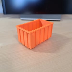 May include: An orange plastic storage bin with a ribbed design. The bin is empty and sitting on a wooden surface.