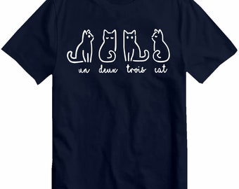 Puede incluir: Una camiseta azul marino con un gráfico blanco de tres gatos y el texto "un deux trois cat".