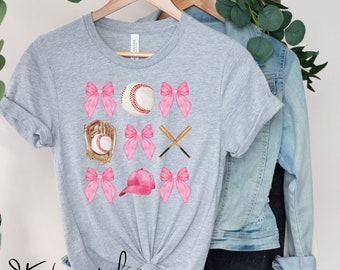 May include: A gray t-shirt with a pink and white baseball themed design. The design includes baseballs, bats, a glove, a hat, and bows.