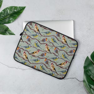 Op de afbeelding: Een groene laptophoes met een herhalend patroon van kleurrijke vogels op takken. De vogels zijn blauwe mezen, roodborstjes en goudvinken.