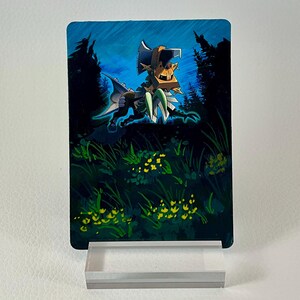 May include: A rectangular trading card featuring a stylized illustration of a creature with a large axe-like head, orange and green armor, and sharp claws, set against a dark blue forest background with yellow flowers in the foreground.