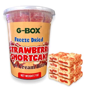 May include: A clear plastic container filled with freeze-dried strawberry shortcake ice cream bites. The container has a label that reads "G-BOX Freeze Dried Strawberry Shortcake Ice Cream Bites" and "NET WEIGHT: 7 OZ". There are also several individual bites of the product stacked on a white surface.
