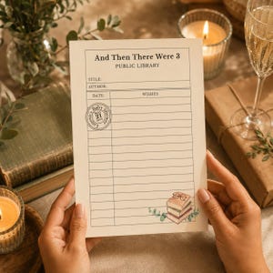 May include: A cream-colored card featuring the text And Then There Were 3 PUBLIC LIBRARY with fields for title, author, date, and wishes. A circular stamp reads Lauren's Baby Shower May 21 20XX, and a small illustration of books with glasses.