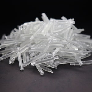 May include: A pile of clear, translucent plastic rods. The rods are approximately 2.5 cm in length and have a slightly rounded end.