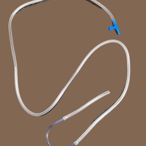 May include: Clear plastic tubing with a blue T-connector. The tubing is curved and flexible, with a smooth surface. The image is set against a brown background.