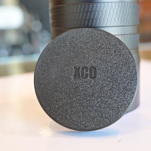 May include: A black lens cap with the word "XCO" printed on it.