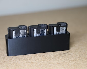 Peut inclure: Un chargeur de batterie en plastique noir avec quatre emplacements pour charger les batteries d'appareil photo. Le chargeur porte l'inscription "Nikon EN-EL15" imprimée sur les batteries.