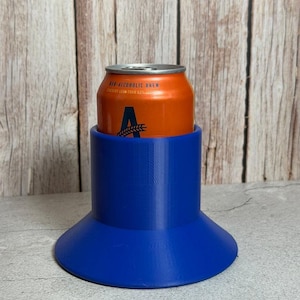 May include: A bright blue cylindrical drink holder with a wide, flared base. An orange aluminum can labeled Non-Alcoholic Brew with a large letter A and a wheat stalk graphic is inserted into the center of the blue holder.