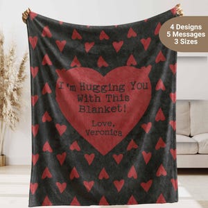 May include: A black fleece blanket with a red heart pattern and a large red heart in the center. The heart has the text "I'm Hugging You With This Blanket! Love, Veronica" printed on it.