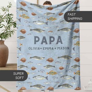 May include: A light blue blanket featuring a pattern of various fish illustrations. The word "PAPA" is displayed in large, gray letters, with the names "OLIVIA, EMMA, MASON" below. The blanket is labeled "SUPER SOFT".