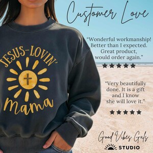 May include: Dark gray sweatshirt with the text "JESUS-LOVIN' Mama" in yellow, featuring a sunburst design with a cross. The sweatshirt has a crew neck and long sleeves. The image also includes customer reviews and the brand name.