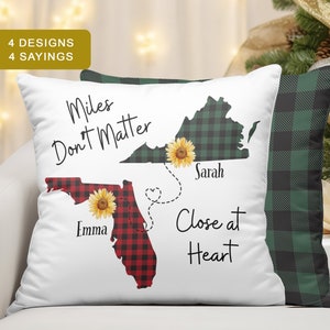 May include: White pillow with a green and black plaid design on the back. The front of the pillow features a red and black plaid outline of Florida with the name "Emma" and a green and black plaid outline of Virginia with the name "Sarah". The text "Miles Don't Matter Close at Heart" is printed on the pillow.