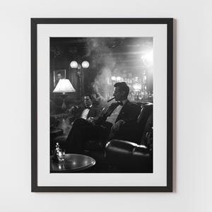 Könnte beinhalten: Schwarz-Weiß-Druck in einem Rahmen, der zwei Personen in Anzügen zeigt, von denen eine eine Zigarre raucht, in einem verrauchten Raum. Die Szene umfasst eine Bar und eine Lampe. Das Bild spielt mit Kontrasten.