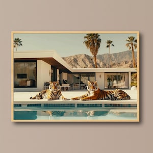 May include: A framed print featuring two tigers resting by a pool in front of a modern house. The tigers have orange and black stripes. Palm trees and mountains are visible in the background. The print has a wooden frame.