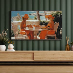 May include: A flat-screen TV displays a vintage-style image of two people in orange outfits and hats, seated at a table. The scene is set outdoors with a coastal backdrop. The TV is mounted above a light wood cabinet.