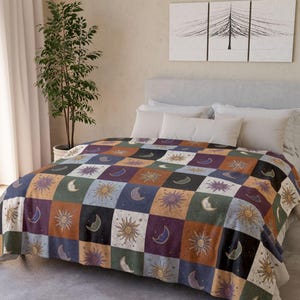 May include: A patchwork quilt with a celestial design of suns, moons, and stars in various colours. The quilt is draped over a bed with white pillows. The quilt's squares are in shades of blue, green, purple, and orange.
