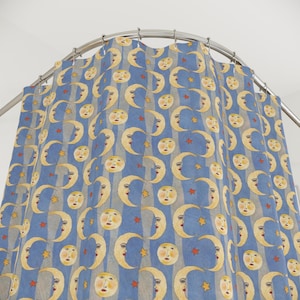 May include: A blue and grey striped shower curtain featuring a repeating pattern of yellow crescent moons with faces and red stars. The curtain hangs from a curved metal rail.