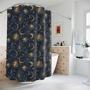 May include: A navy blue shower curtain with a celestial pattern. Gold suns, moons, and stars are printed across the fabric. The curtain hangs from a silver rail in a bathroom.